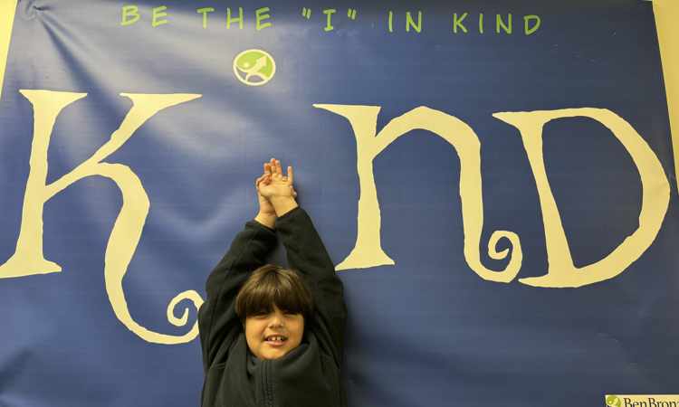 Young male students standing in front of banner with the word "Kind."