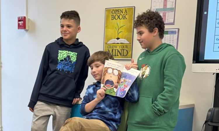 3 students, one holds up a book showing pages to other students.